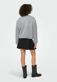 Sweatshirt gris à coupe décontractée, jupe noire évasée et bottes noires en cuir jusqu'aux genoux avec des accents de boucles. Look texturé et décontracté.