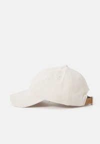 Cappellino da baseball in corduroy beige con visiera leggermente curvata, cintura regolabile sul retro e dettagli cuciti sul fronte.