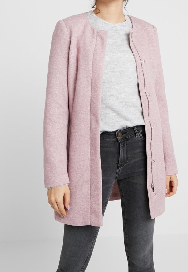 Lichtroze wolmixjas met een recht ontwerp, lange mouwen en een drukknopen sluiting. Gemaakt over een grijze trui en donkere jeans.