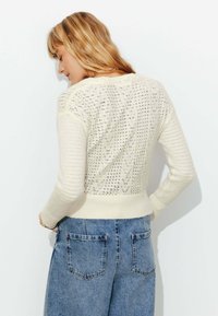 Pull tricoté en écru avec un dos texturé et à motifs, et un ourlet côtelé, associé à un jean en denim bleu taille haute.