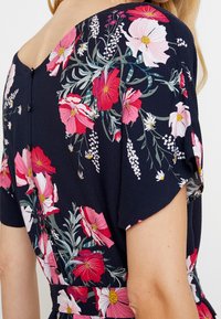 Blumenmusterkleid mit navyblauem Hintergrund, pinken und weißen Blumen, kurzen Ärmeln und Knopfdetails entlang des Rückens. Strukturierten Stoff.