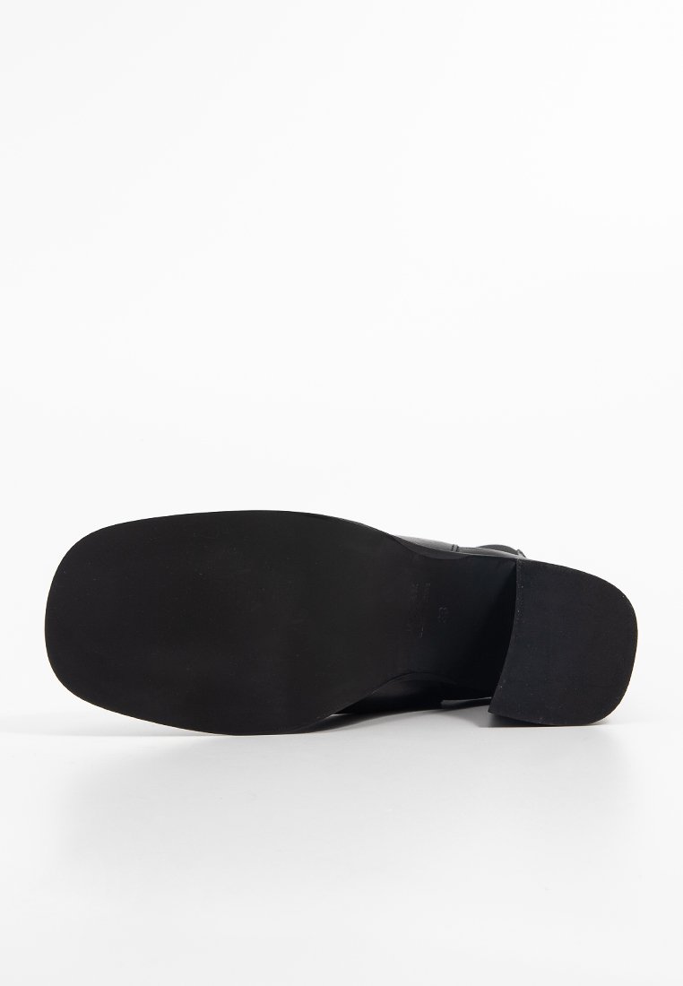 Semelle de chaussure noire avec un design plat, texture lisse et crampons minimaux. Bout légèrement arrondi et talon effilé. Apparence simple et fonctionnelle.