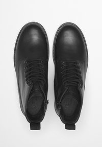 Czarne skórzane botki na kostkę z okrągłymi noskami, wiązane z przodu, o fakturowanej powierzchni i z pętelką przy pięcie ułatwiającą zakładanie.