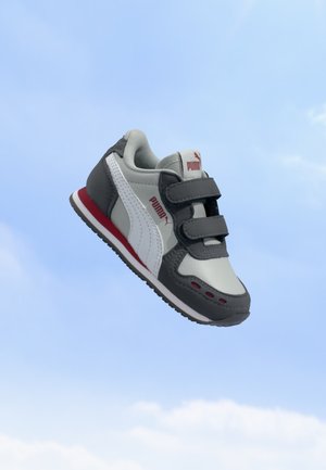 Γκρι και λευκό αθλητικό παπούτσι Puma με κόκκινες λεπτομέρειες και δύο λουριά με βέλκρο, εμφανίζεται με φόντο έναν καθαρό γαλάζιο ουρανό.