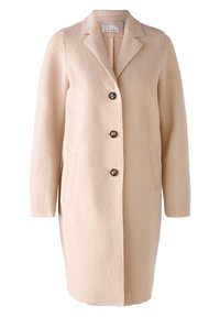 Abrigo de lana beige con cuello de muesca, mangas largas, bolsillos frontales y tres botones marrones. Textura suave con detalles mínimos.