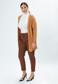 Brune høj talje bukser parret med en cremefarvet rullekravebluse og en tekstureret, kabel-strikket, åbent front karamel cardigan. Sorte sko med udsmykninger.