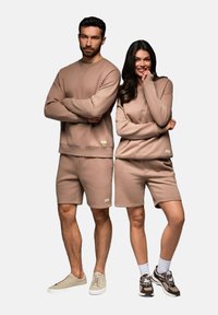 Set di felpe e pantaloni corti casual in cotone beige, caratterizzato da un collo rotondo, polsini a coste e un discreto logo sul bordo inferiore.