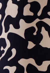 Des formes abstraites irrégulières noires et beiges formant un motif lisse, semblable à un camouflage, sur une surface textile texturée.