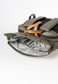 Zaino verde oliva con parte superiore nera, dettagli in pelle e interno grigio chiaro. Presenta una tasca con zip e spallacci regolabili.