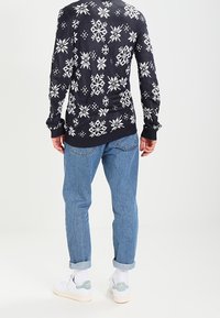 Pull bleu marine avec motif de flocons de neige blancs, associé à un jean bleu clair. Comprend des ourlets retroussés et des baskets blanches avec des accents verts.