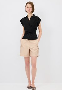 Blusa corta de manga corta negra con cierre de botones, combinada con pantalones cortos de cargo beige; incluye bolsillos y un ajuste relajado. Bailarinas de estampado animal completan el look.