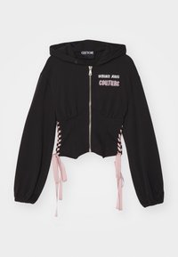Čierna skrátená mikina s kapucňou a zipsom, ružové šnúrky na bočných stranách a logo "Versace Jeans Couture" v ružovej a bielej farbe na hrudi.