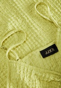 Robe texturée vert lime avec des bretelles fines, présentant un motif froissé et une étiquette noire avec "JJXX" près de l'encolure.