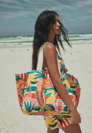 Värikäs kangaskassi, jossa on trooppisia hedelmä- ja lehtikuvioita; valmistettu kankaasta, jossa paksut ja kontrastiset hihnat; tilava malli ranta-aktiviteetteihin.