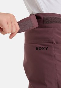 Bordeauxfarbene Skihosen mit strukturiertem Bund, der mit Klettverschluss versehen ist. Das Roxy-Logo ist in schwarz auf der rechten Seite gestickt. Glatte Stoffqualität.