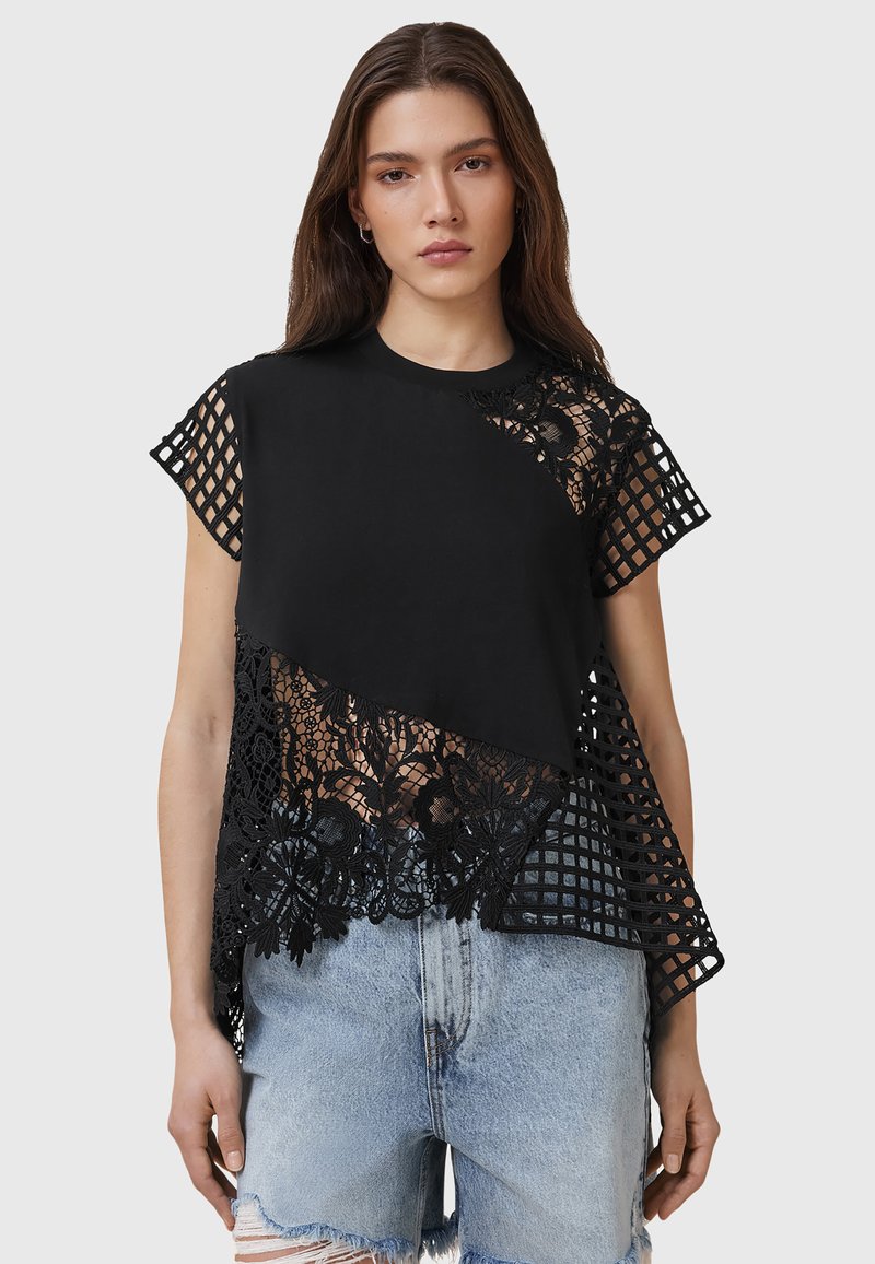 Top nero con un design a rete e a griglia testurizzato, taglio asimmetrico, maniche corte e scollatura rotonda, abbinato a pantaloni shorts in denim sfrangiati.