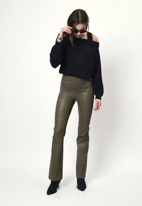 Zwarte off-the-shoulder trui met lange mouwen, gecombineerd met olijfgroene aansluitende leren broek en zwarte enkellaarsjes.