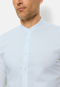 Witte blouse met bandkraag, gemaakt van soepele stof. Voorzien van een voorpaneel met vier knopen, minimale textuur.