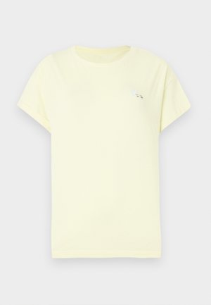 Απλή ανοιχτό κίτρινη κοντομάνικη μπλούζα με μια μικρή λευκή καρδιά και μαύρη λεπτομέρεια κειμένου στην πάνω αριστερή πλευρά του στήθους.