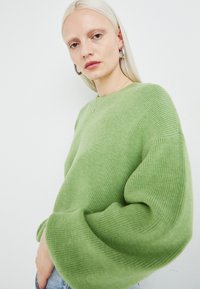 Grønn ribbestrikket genser med overdimensjonerte ermer, med rund hals og myk tekstur; kombinert med denimjeans.