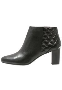 Bottines en cuir noir avec un bout pointu, un détail latéral matelassé et un talon épais, présentant une texture lisse et un design épuré.