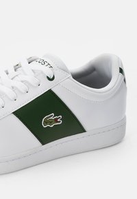 Vit sneaker med mörkgrönt sidofält och broderad krokodillogo, vita skosnören och vadderad krage.