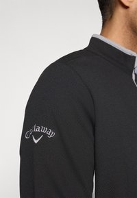 Mustmust mustmustiga performantsi pullover, millel on tekstureeritud kangas, hall kraeakkent ja tikitud "Callaway" logo vasakul varrukal.