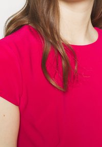 Fuchsiová krátká halenka s kulatým výstřihem, vyrobená z hladké tkaniny, která se vyznačuje jednoduchým designem bez dalších vzorů nebo akcentů.