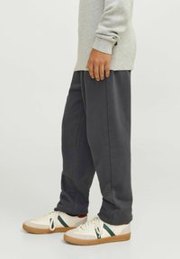 Grå sweatshirt med långa ärmar, i kombination med mörkblå joggingsbyxor. Skorna är vita med gröna och röda detaljer, och har en gummisula.