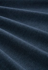 Donkerblauwe stof met een zachte textuur en subtiel visgraatpatroon, met gevouwen lagen die diepte en dimensie creëren.