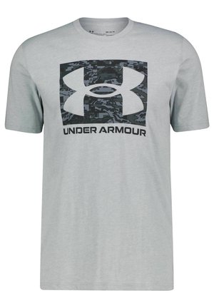 Lys grå T-shirt med korte ærmer med en stor sort camouflage Under Armour-logo og teksten "UNDER ARMOUR" centreret på forsiden.