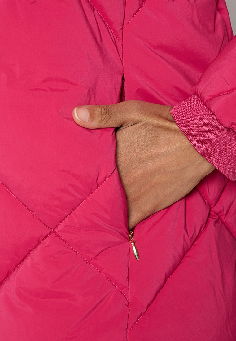 Rosa gesteppte Jacke mit einem Reißverschlussfach, elastischen Bündchen und einem rautenförmigen Steppmuster. Weiche, glatte Textur sichtbar.