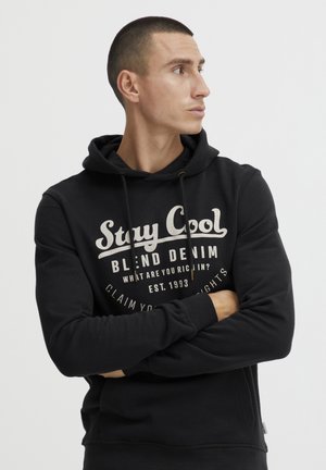 Black cotton hoodie featuring a printed logo in cream, adjustable drawstrings, and ribbed cuffs. Side tag detail near hem.