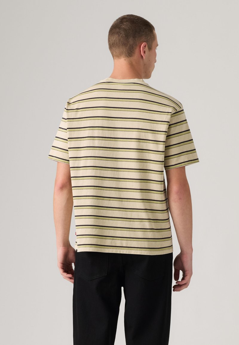 Man facing away wearing a beige short-sleeve shirt with thin black and yellow horizontal stripes and black pants.