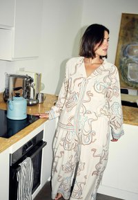 Set de pijamale deschise la culoare cu imprimeu cu caracatiță, guler șal, mâneci lungi și talie elastică. Fundal de bucătărie cu ceainic.