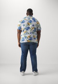 Lyhythihainen valkoinen trooppinen paita, jossa värikkäitä kukka- ja lehtikuvioita, yhdistetty sinisiin farkkuihin ja valkoisiin tennareihin.