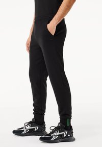 Zwarte joggingsbroek van zacht materiaal, met zijzakken, een aangesloten boord en een klein logo op de voorkant.