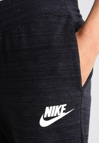 Svarta träningsbyxor i texturerad tyg med mjuk känsla. Har en vit Nike-logga på vänster ben och en sidficka.