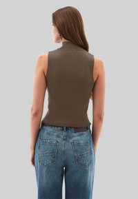 Mouwloze bruine top gemaakt van gebreide stof met een hoge kraag, gecombineerd met blauwe high-waisted denim jeans met achterzakken.