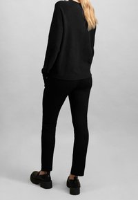 Felpa nera con maniche lunghe e orlo a coste, abbinata a pantaloni neri aderenti. Footwear con suola spessa e design slip-on.