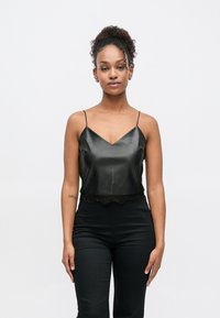 Top scurt din satin negru cu decolteu în V și bretele subțiri; are un bordaj din dantelă de-a lungul marginii inferioare. Asortat cu pantaloni negri cu talie înaltă.