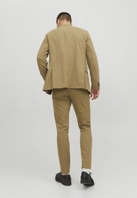 Khaki kostymjacka och byxor i slät tyg, med en skräddarsydd passform och subtil textur, i kombination med svarta skor.