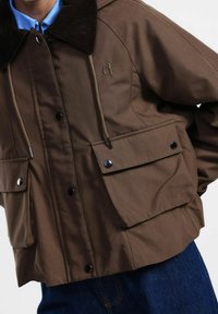 Giacca esterna marrone con colletto in corduroy, bottoni a pressione e due tasche frontali. Realizzata in un tessuto morbido con una vestibilità comoda.