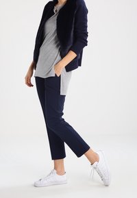 Námořnický modrý, texturovaný cardigan přes šedou košili, v kombinaci s tmavými kalhotami a bílými teniskami, zdůrazňující příležitostní, vrstvené oblečení.