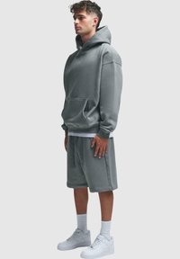 Grå oversized hettegenser med kengurulomme og matchende shorts, laget av myk stoff. Båret med hvite sneakers og ankelstrømper.