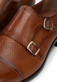 Zapatos de cuero marrón con un patrón de espiga texturizado, detalles de doble hebilla y un diseño de punta redondeada.
