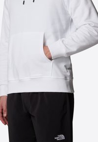 Vit bomulls hoodie med en framficka och ribbade ärmar, bärs tillsammans med svarta shorts med en logotyp på vänster lår.