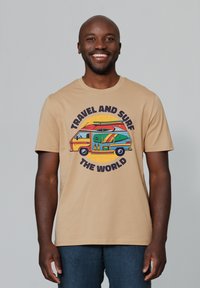 Beige katoenen t-shirt met een kleurrafische afbeelding van een bus met surfplanken, met de tekst "REIS EN SURF DE WERELD" in vette letters.