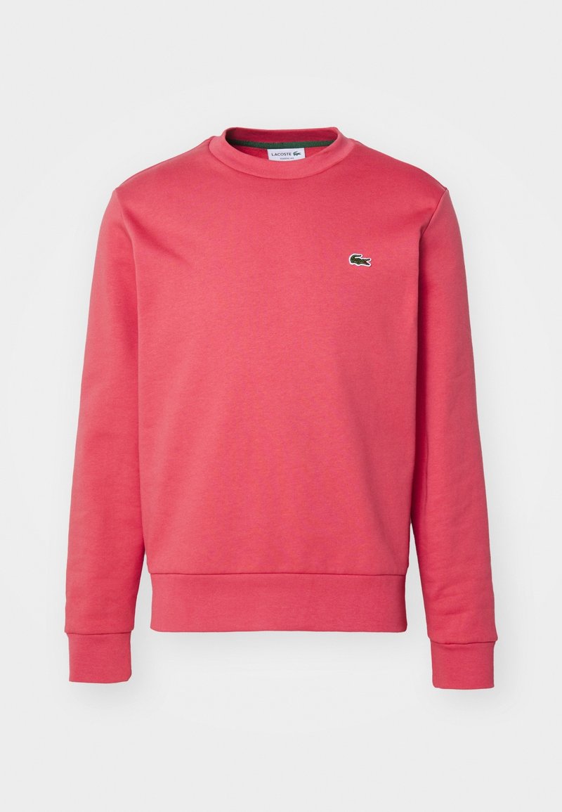Sweat-shirt corail à manches longues avec col rond, poignets et ourlet côtelés, arborant un petit logo crocodile vert sur la poitrine gauche.