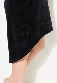 Schwarzer, weicher Stoffrock mit asymmetrischem Saum, der eine glatte Textur und einen leichten Glanz aufweist und ein minimalistisches Design präsentiert.